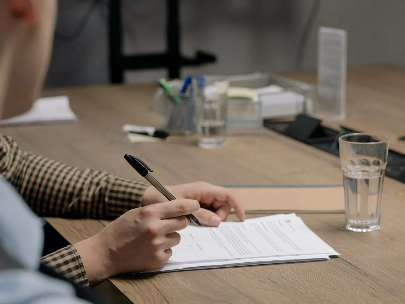Una persona firmando un documento sobre la mesa de un despacho, con un bolígrafo en la mano