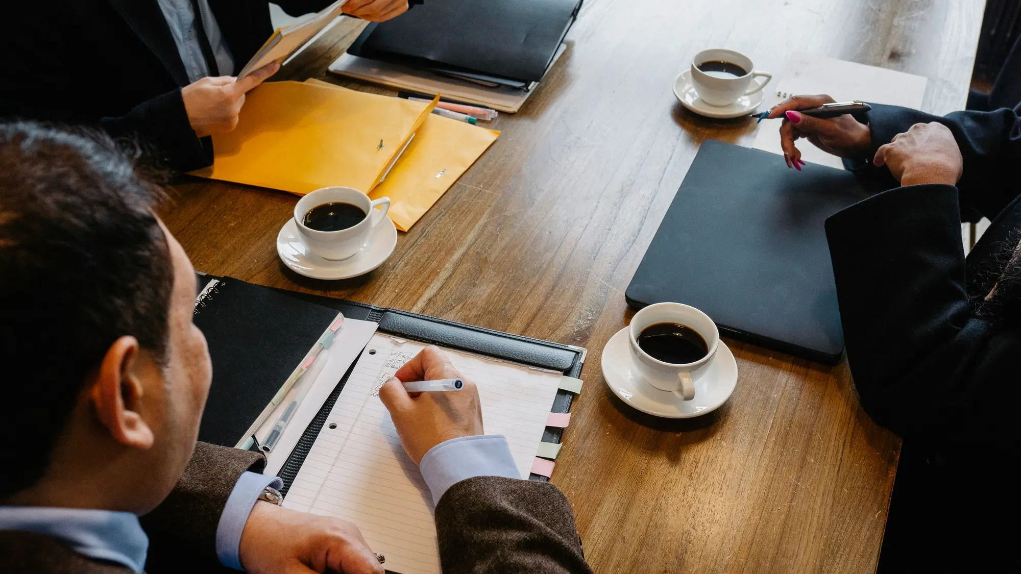 Vista cenital de una mesa de reuniones con documentos, cuadernos y tazas de café durante una reunión