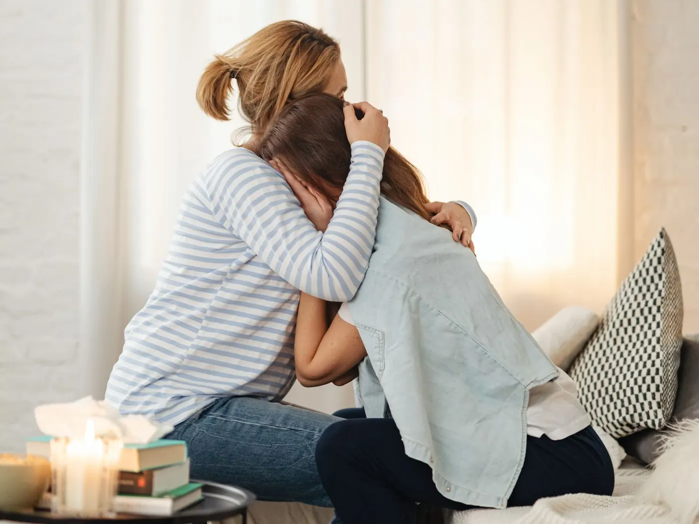 Una madre abraza a su hija sentadas en el sofá del salón